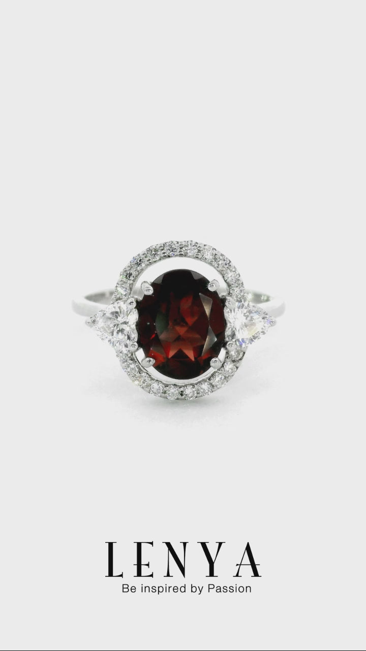 LENYA แหวนโกเมน (Garnet)  สีแดงแก่ก่ำ ช่วยปกป้องคุ้มครอง และช่วยให้สมปรารถนาในเรื่องหน้าที่การงาน การเงินและเรื่องความรัก ล้อมรอบด้วยคิวบิคเซอร์โคเนีย 22 เม็ด บนตัวเรือนเงินแท้ 925 ชุบทองคำขาว